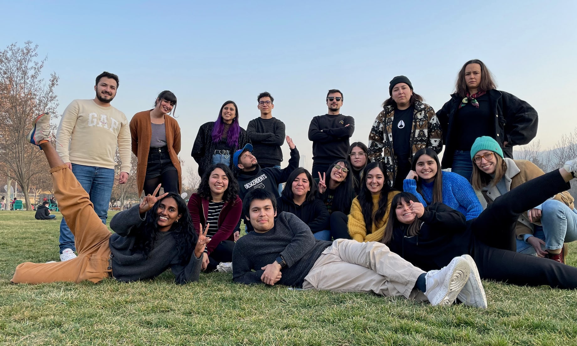 The product design team posed on the grass in a park, two rows of them with a few lying across the front, peace signs and grins, bare winter trees and hills behind.