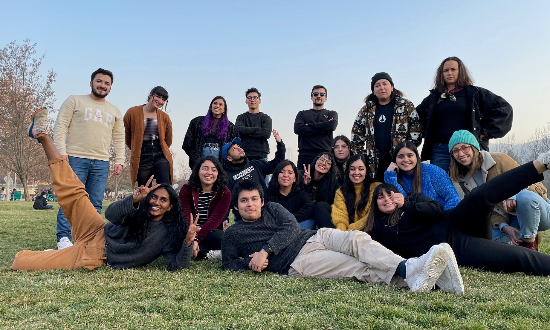 The product design team posed on the grass in a park, two rows of them with a few lying across the front, peace signs and grins, bare winter trees and hills behind.