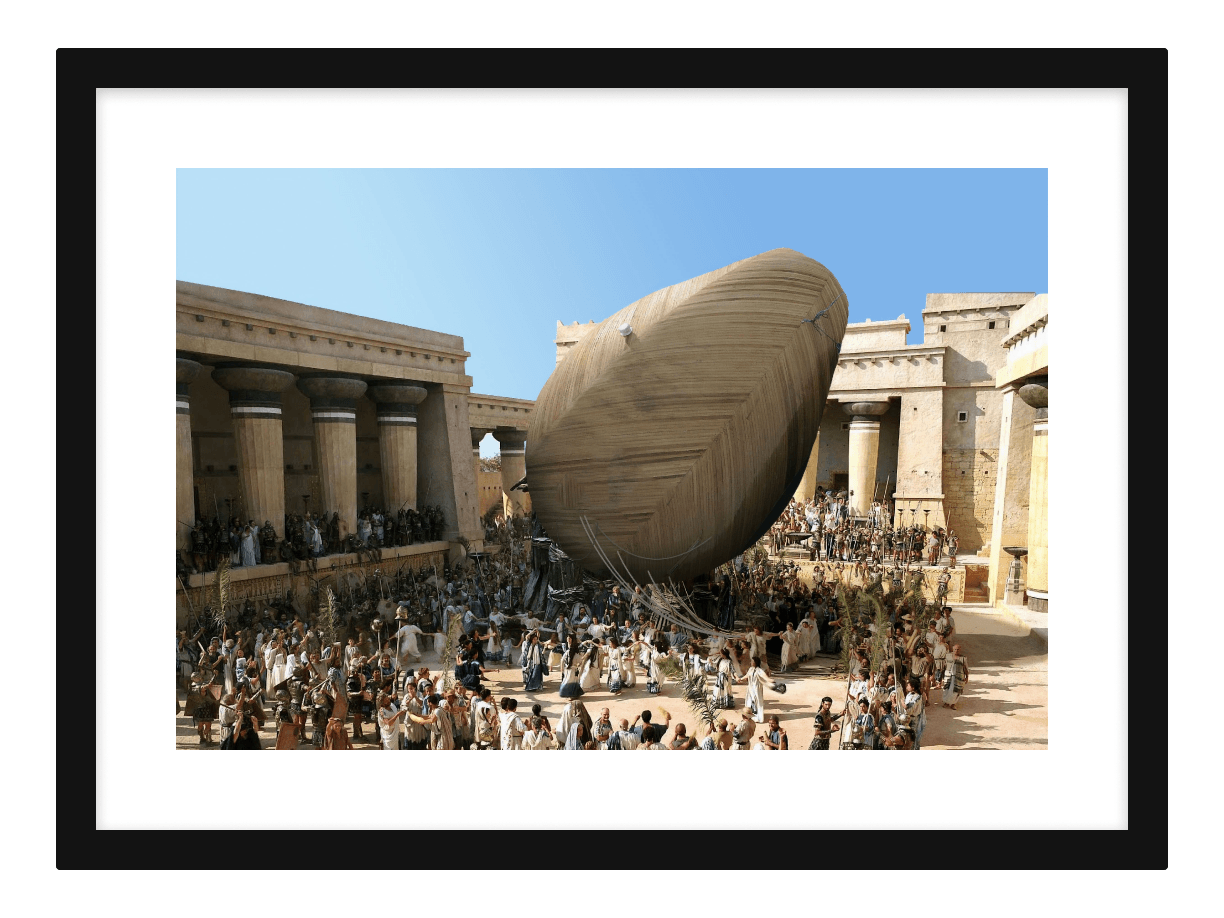 A framed painting of Troy: crowds in the square dragging a giant wooden avocado through the gates where the horse should be.